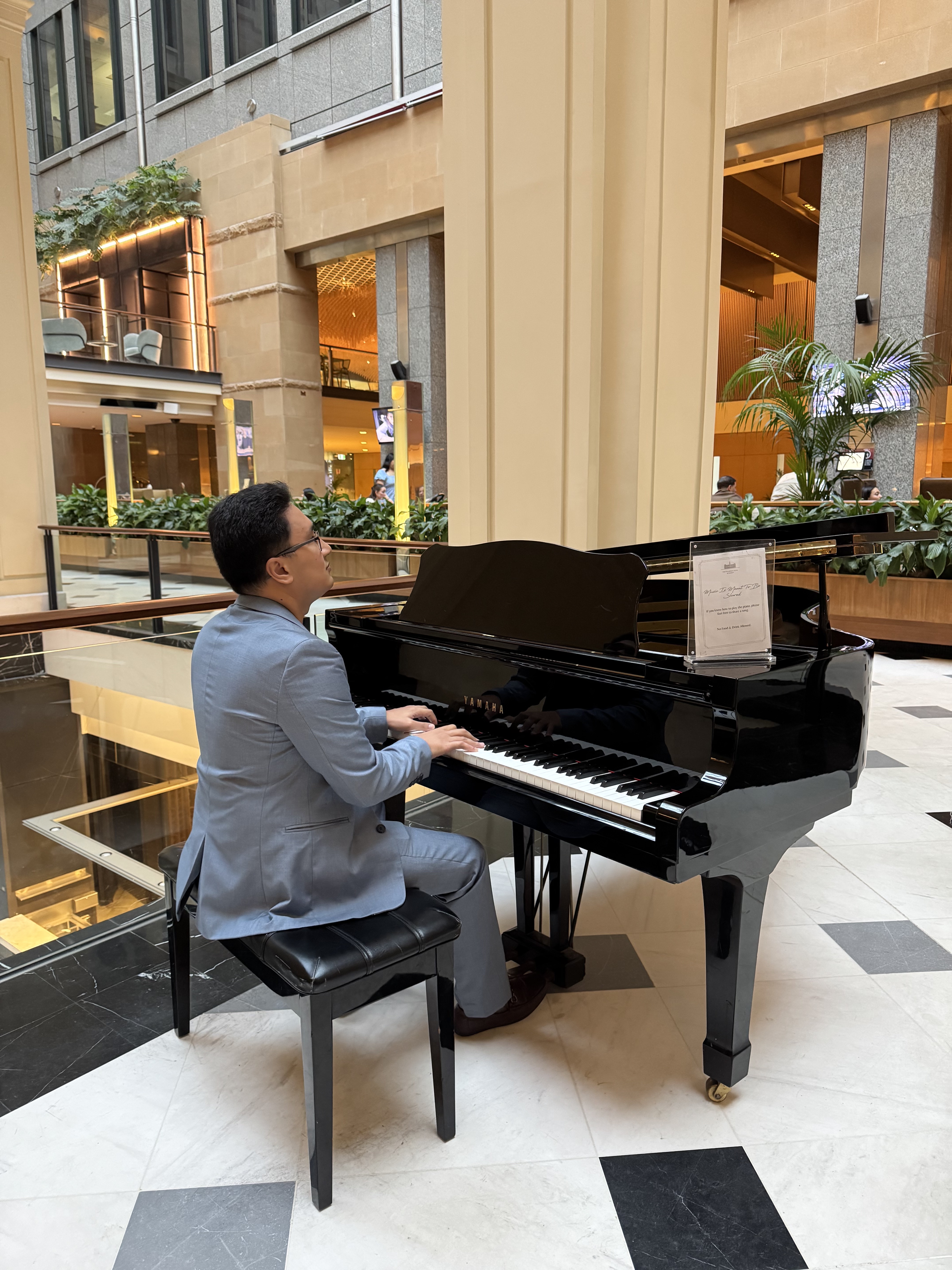 Claro playing a black grand piano in the brightly lit lobby of the Fullerton Hotel